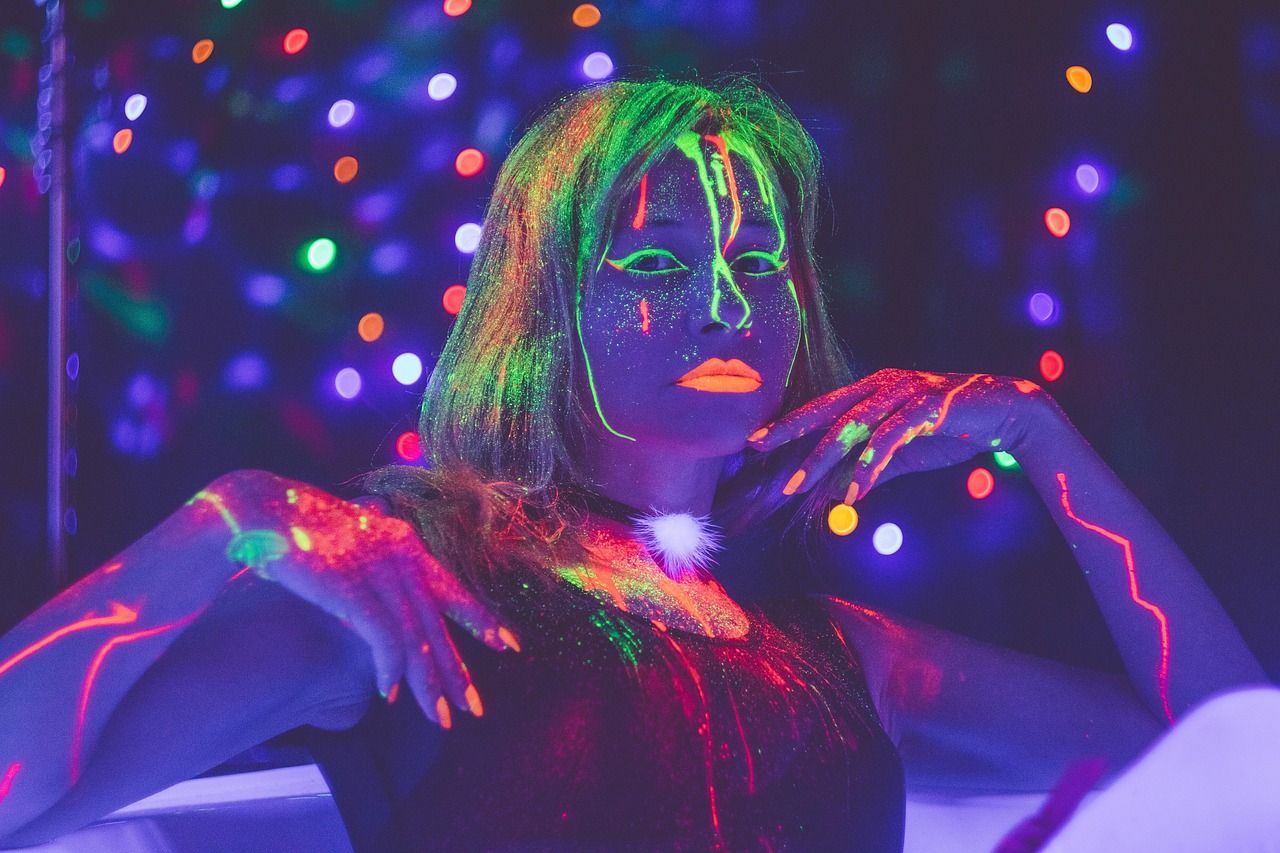 Fotobudka UV — neonowy portret w świetle ultrafioletowym: fluorescencyjne farby fluo świecą na twarzy i dłoniach uczestniczki imprezy